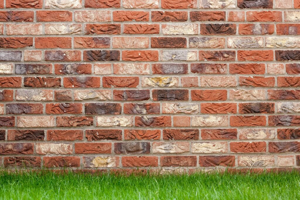 A textured red brick wall with fresh green grass at the base, ideal for backgrounds.